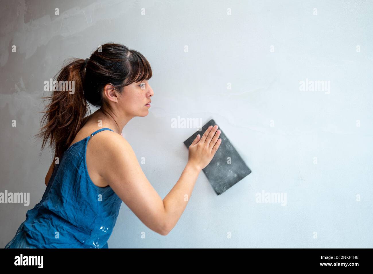 La femme latine répare le mur blanc à l'aide de papier de verre Banque D'Images