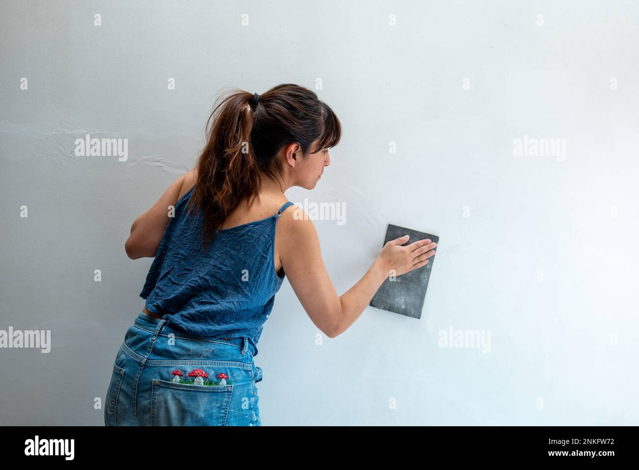 La femme bolivienne répare le mur blanc à l'aide de papier de verre Banque D'Images