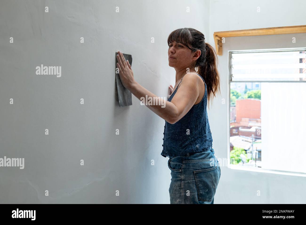 Une femme hispanique répare le mur blanc à l'aide de papier de verre Banque D'Images