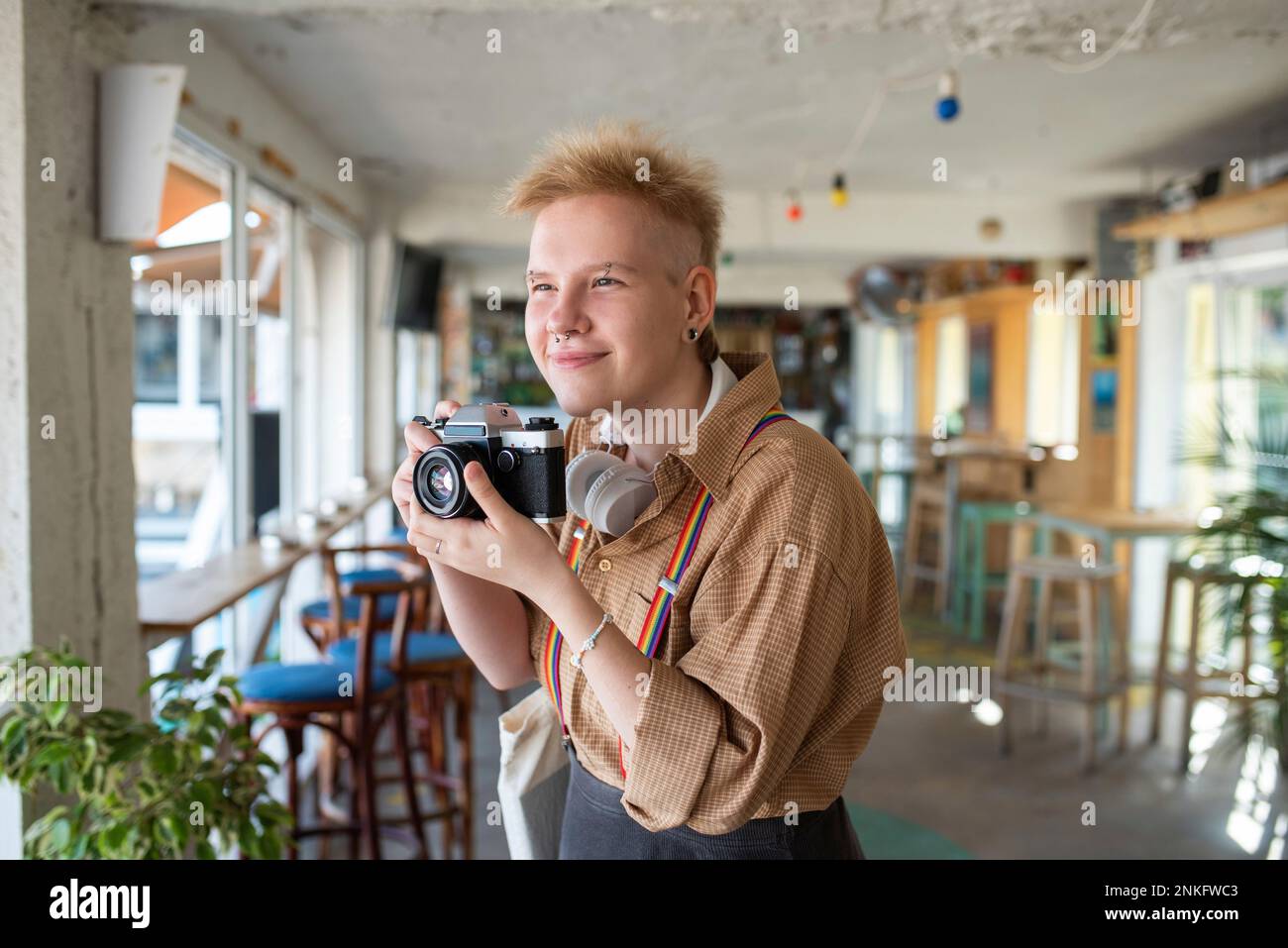 Personne souriante non binaire tenant l'appareil photo pour prendre des photos dans un café Banque D'Images