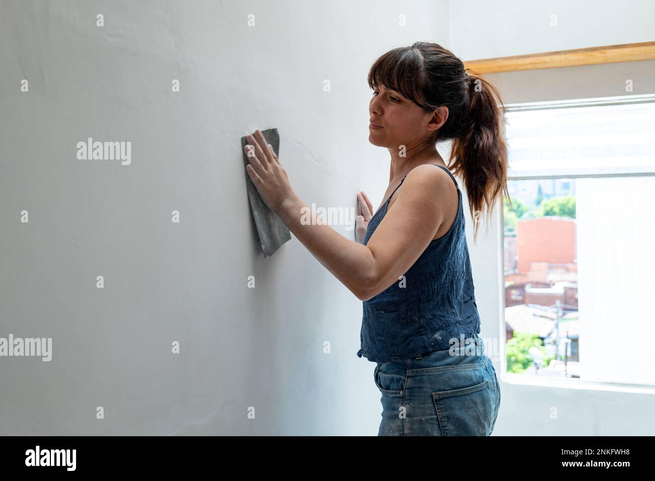 La femme bolivienne répare le mur blanc à l'aide de papier de verre Banque D'Images