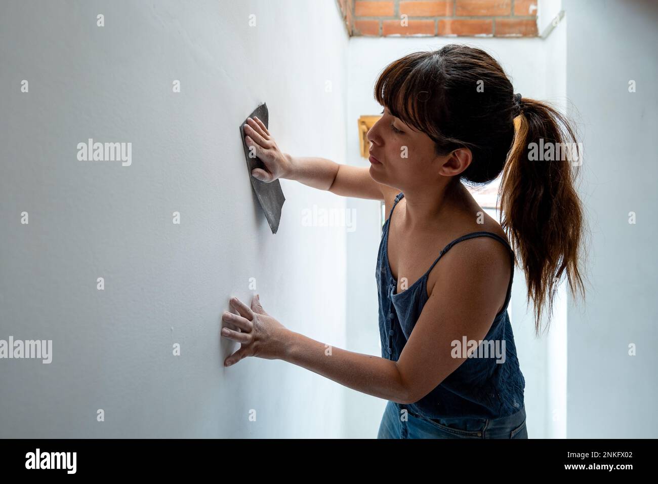 La femme bolivienne répare le mur blanc à l'aide de papier de verre Banque D'Images