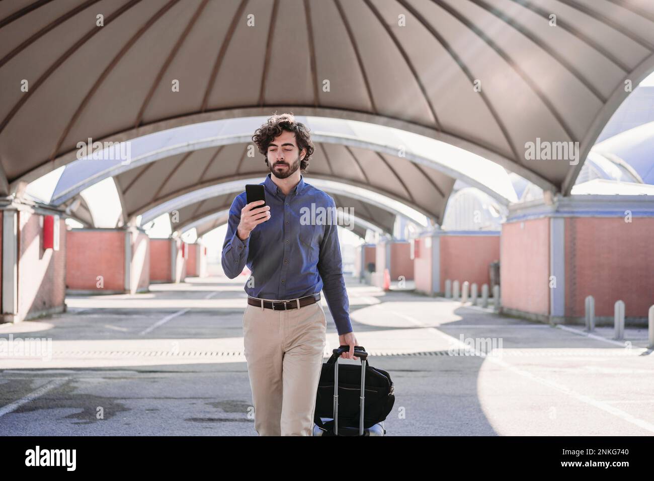 Jeune homme d'affaires marchant avec des bagages et utilisant un smartphone Banque D'Images