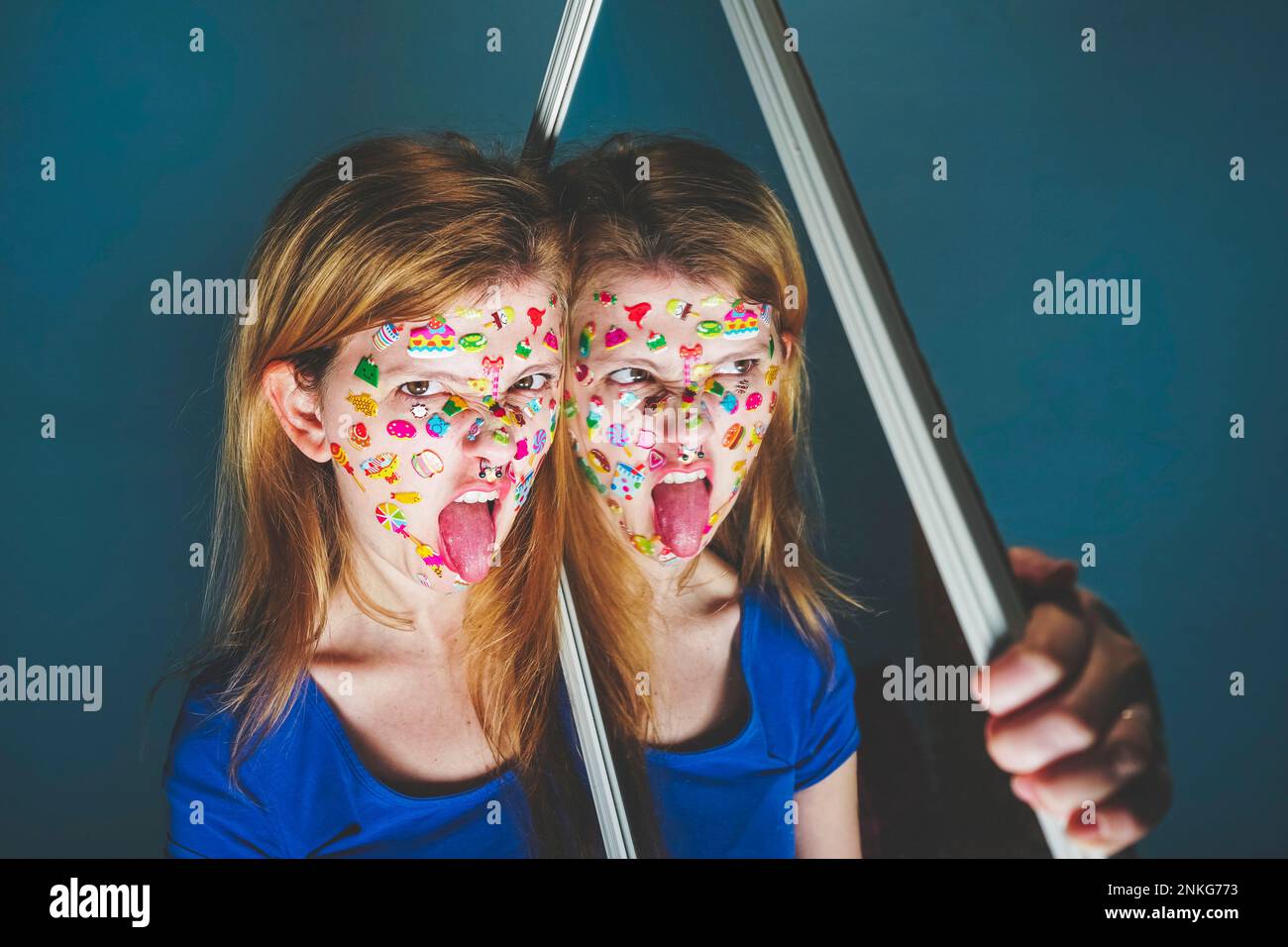 Femme avec miroir collant la langue sur fond bleu Banque D'Images