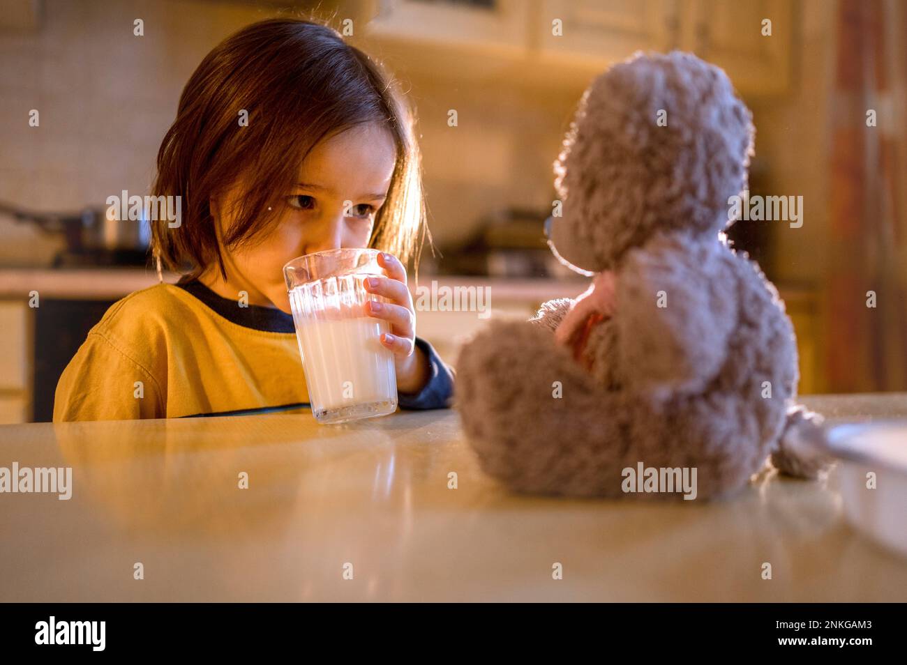 Garçon regardant l'ours en peluche sur une table buvant du lait Banque D'Images