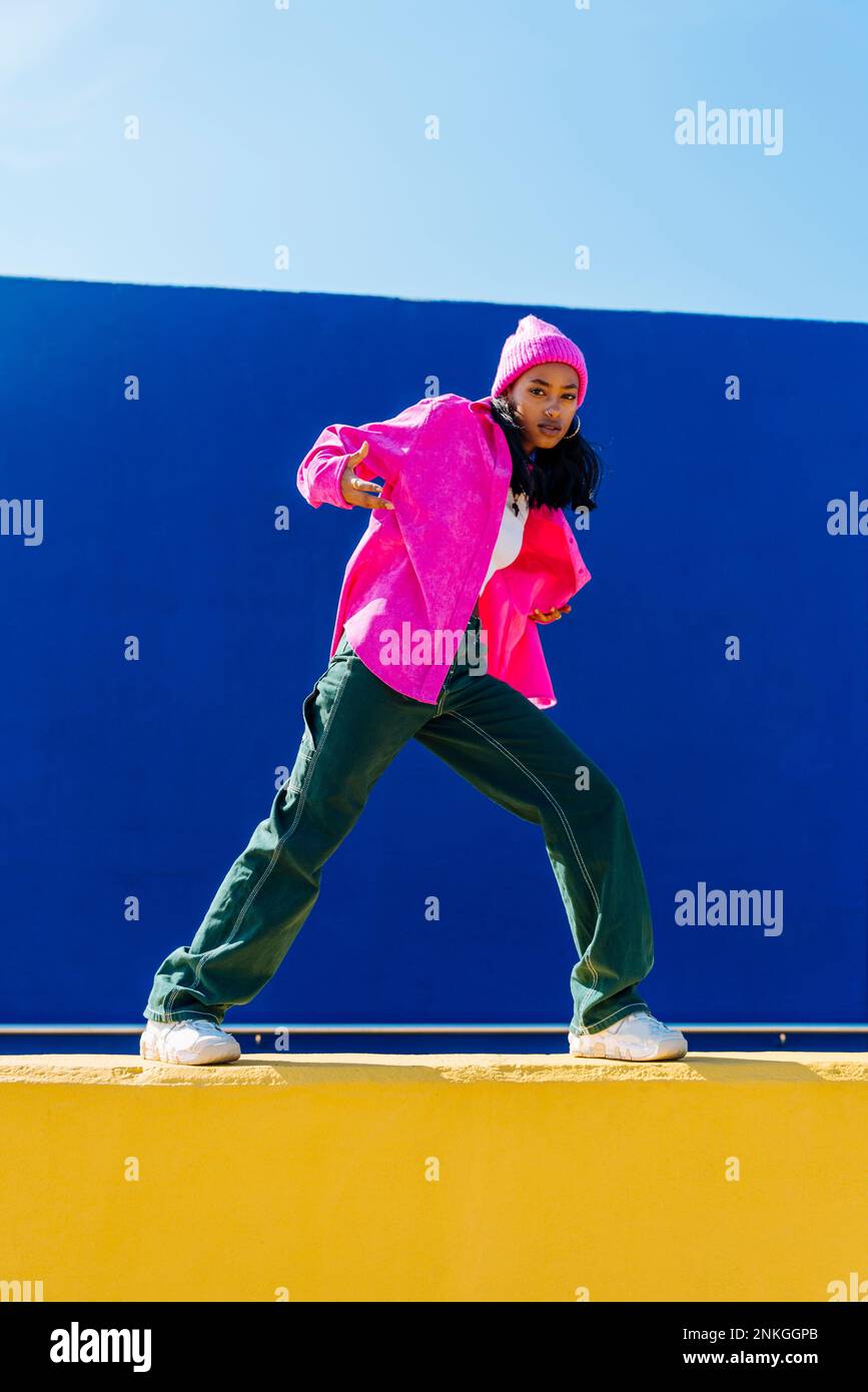 Jeune femme portant une veste rose faisant de la danse hip hop sur le mur Banque D'Images