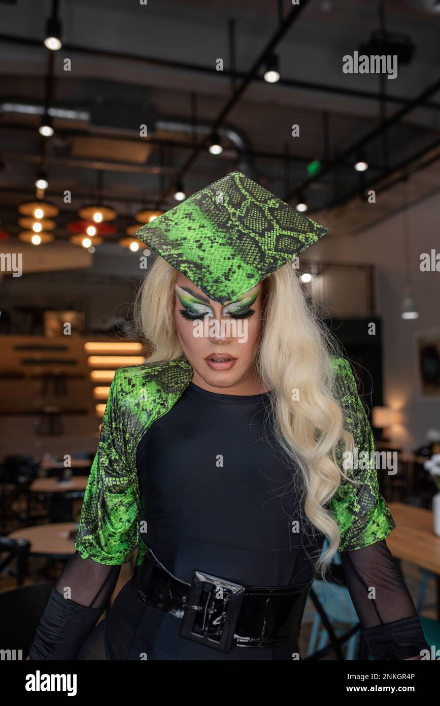 Jeune blonde drag queen avec chapeau vert dans le café Banque D'Images