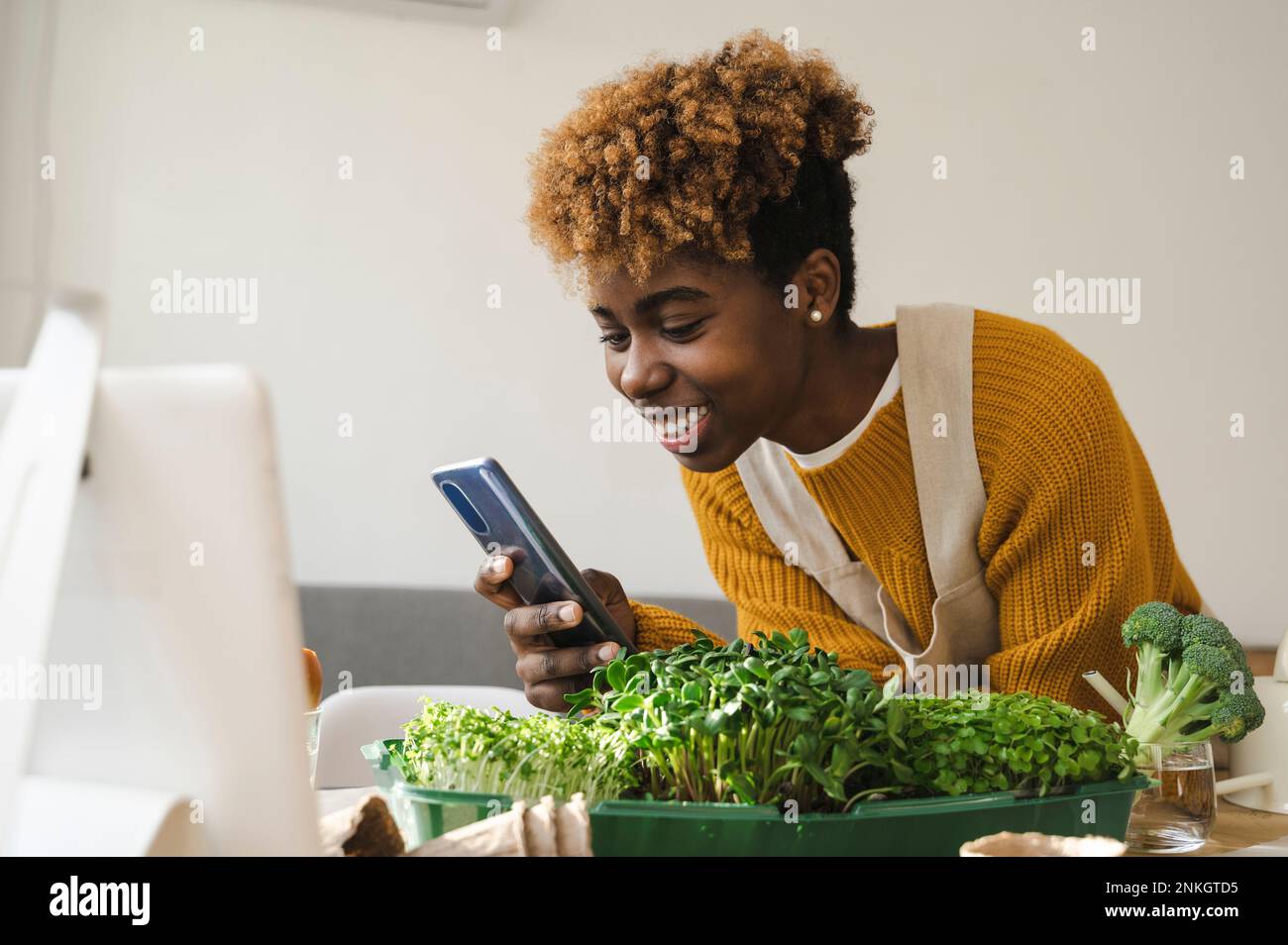 Un jeune blogueur heureux filmant de petits légumes en pleine croissance grâce à un smartphone Banque D'Images