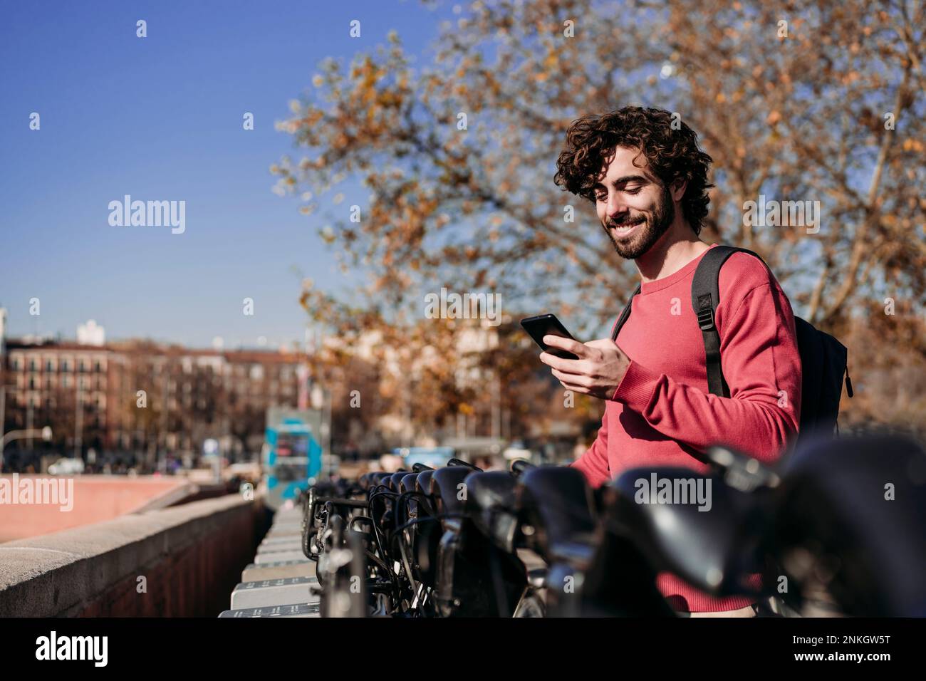 Un homme heureux utilisant l'application mobile pour louer un scooter électrique par beau temps Banque D'Images