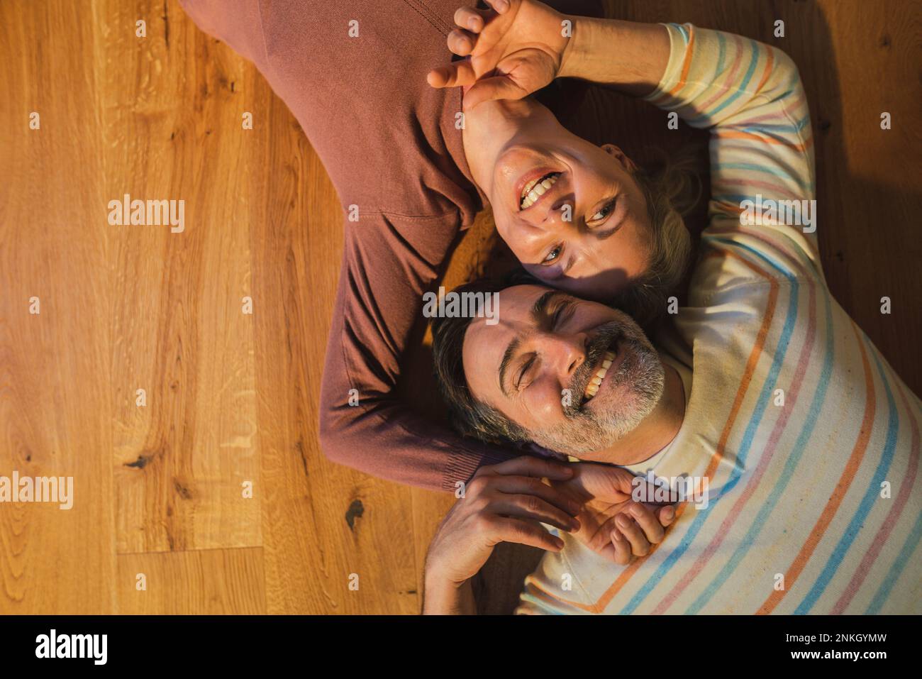 Couple souriant couché sur un sol en bois dur à la maison Banque D'Images