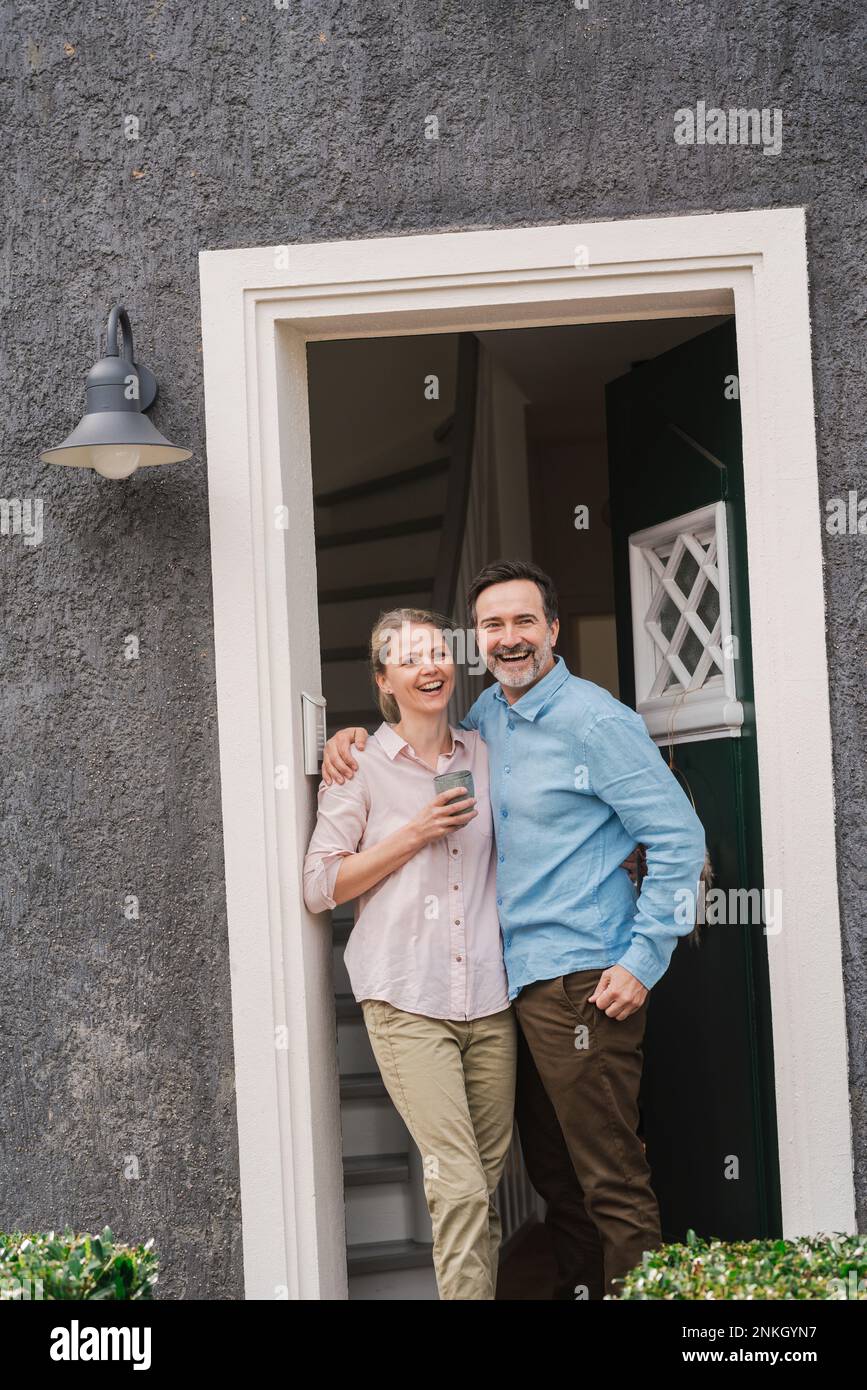 Couple d'âge mûr et gai debout à l'entrée de la maison Banque D'Images