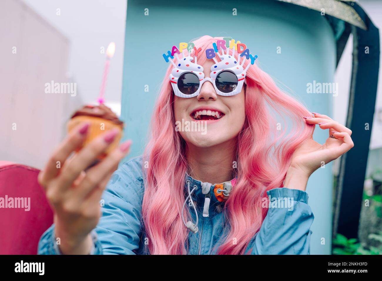 Bonne femme portant des lunettes de fantaisie tenant un cupcake pour fêter son anniversaire Banque D'Images