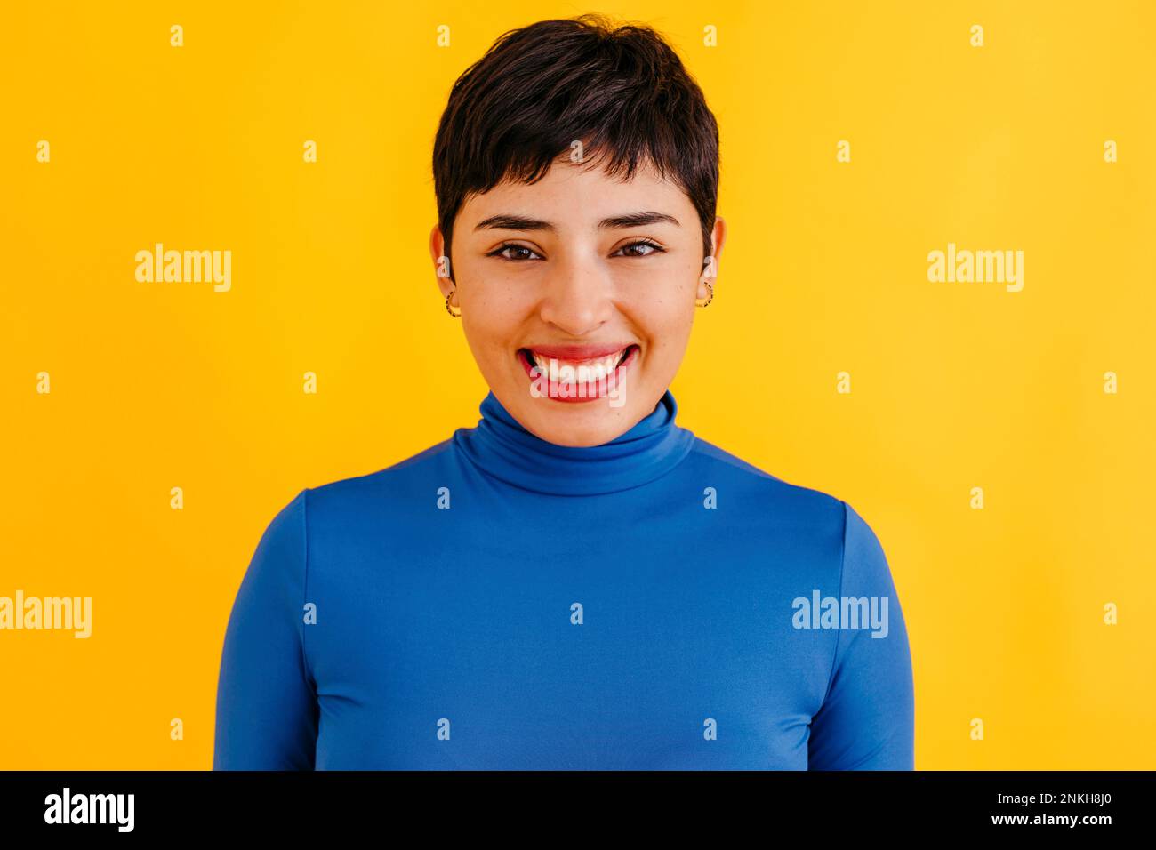 Bonne jeune femme avec la coupe de cheveux de pixie debout sur fond jaune Banque D'Images