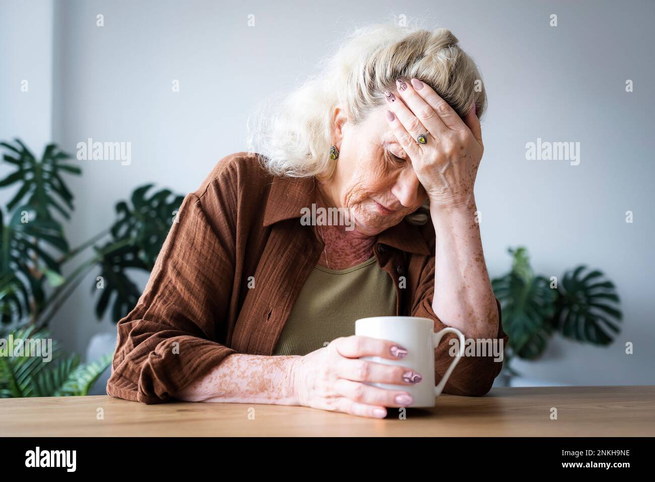Bouleverser la femme âgée avec la tête dans la main assise à la maison Banque D'Images