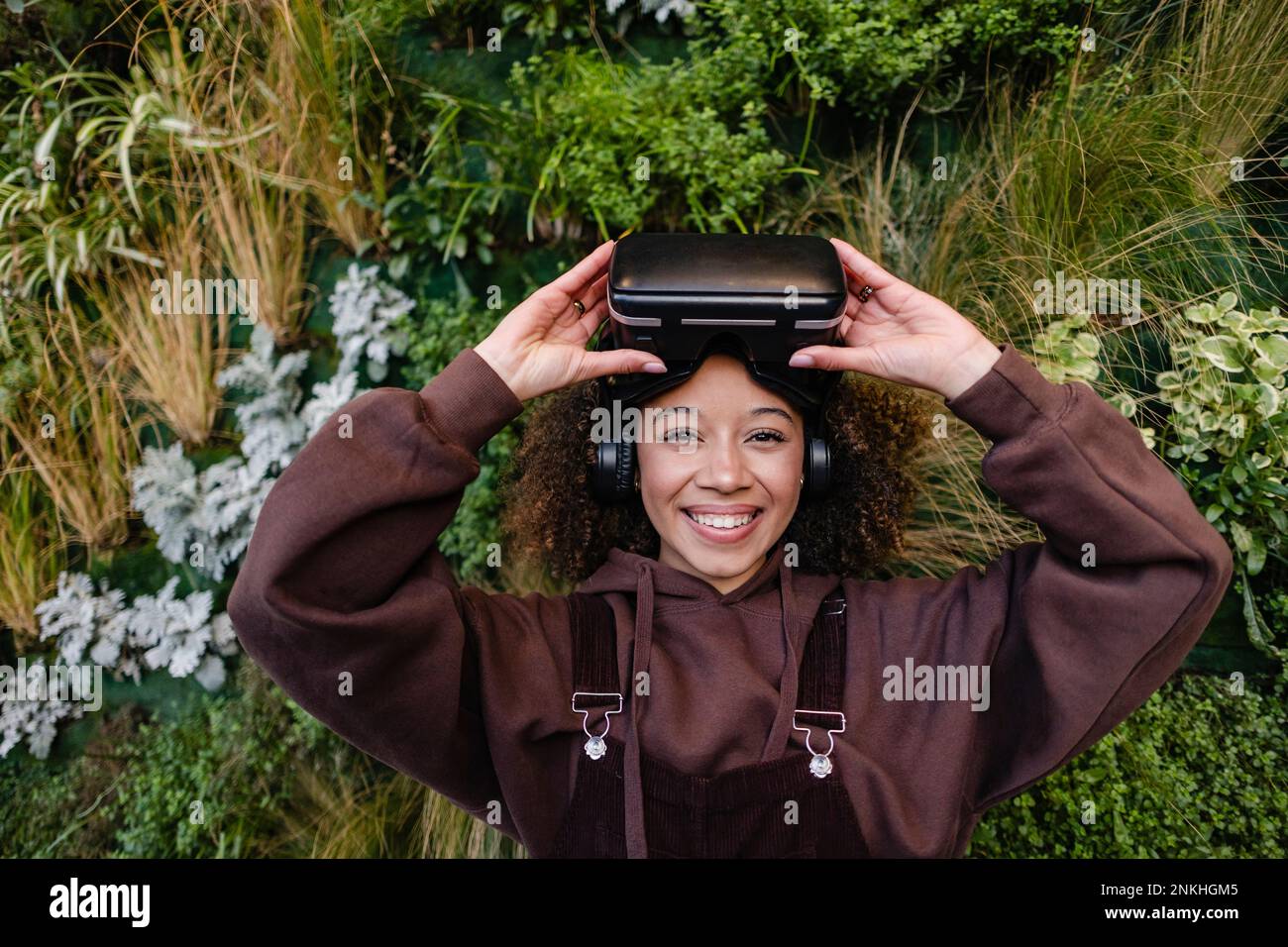 Femme souriante avec lunettes VR devant les plantes Banque D'Images