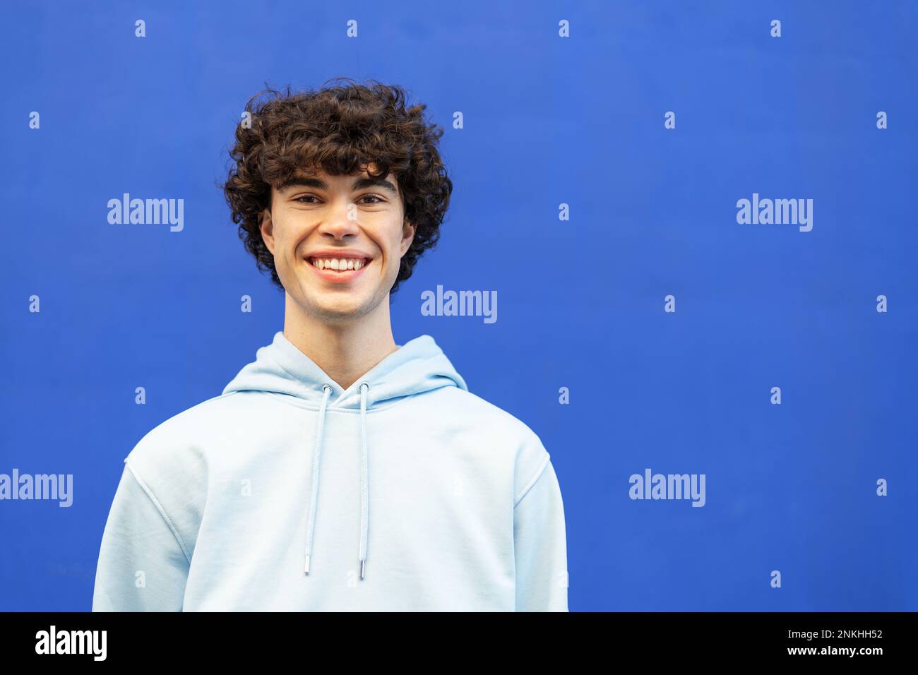 Jeune homme souriant debout devant le mur bleu Banque D'Images