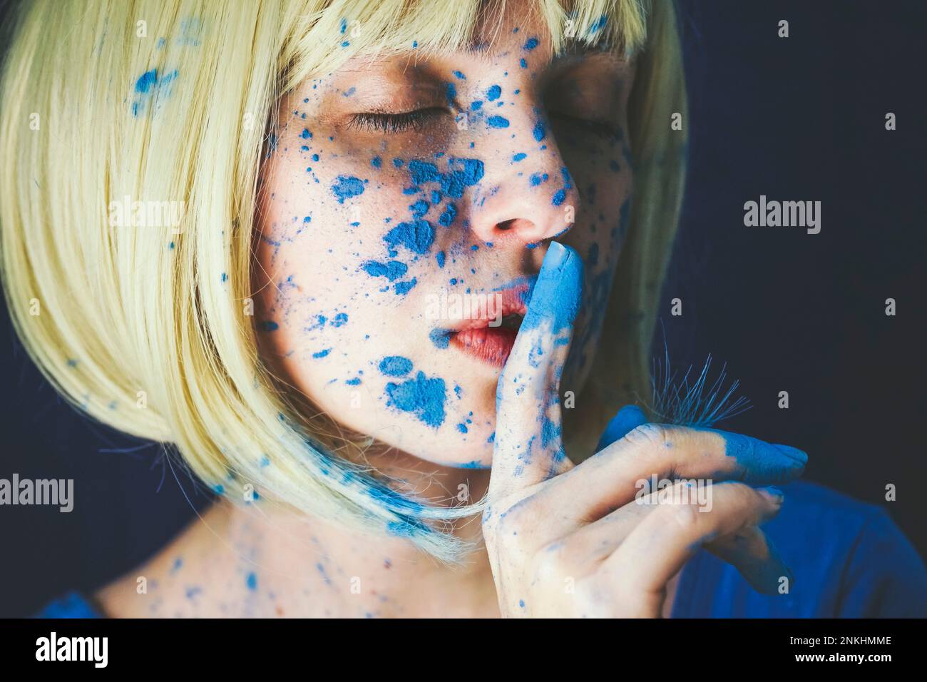 Femme avec peinture en poudre bleue et doigt sur les lèvres sur fond noir Banque D'Images