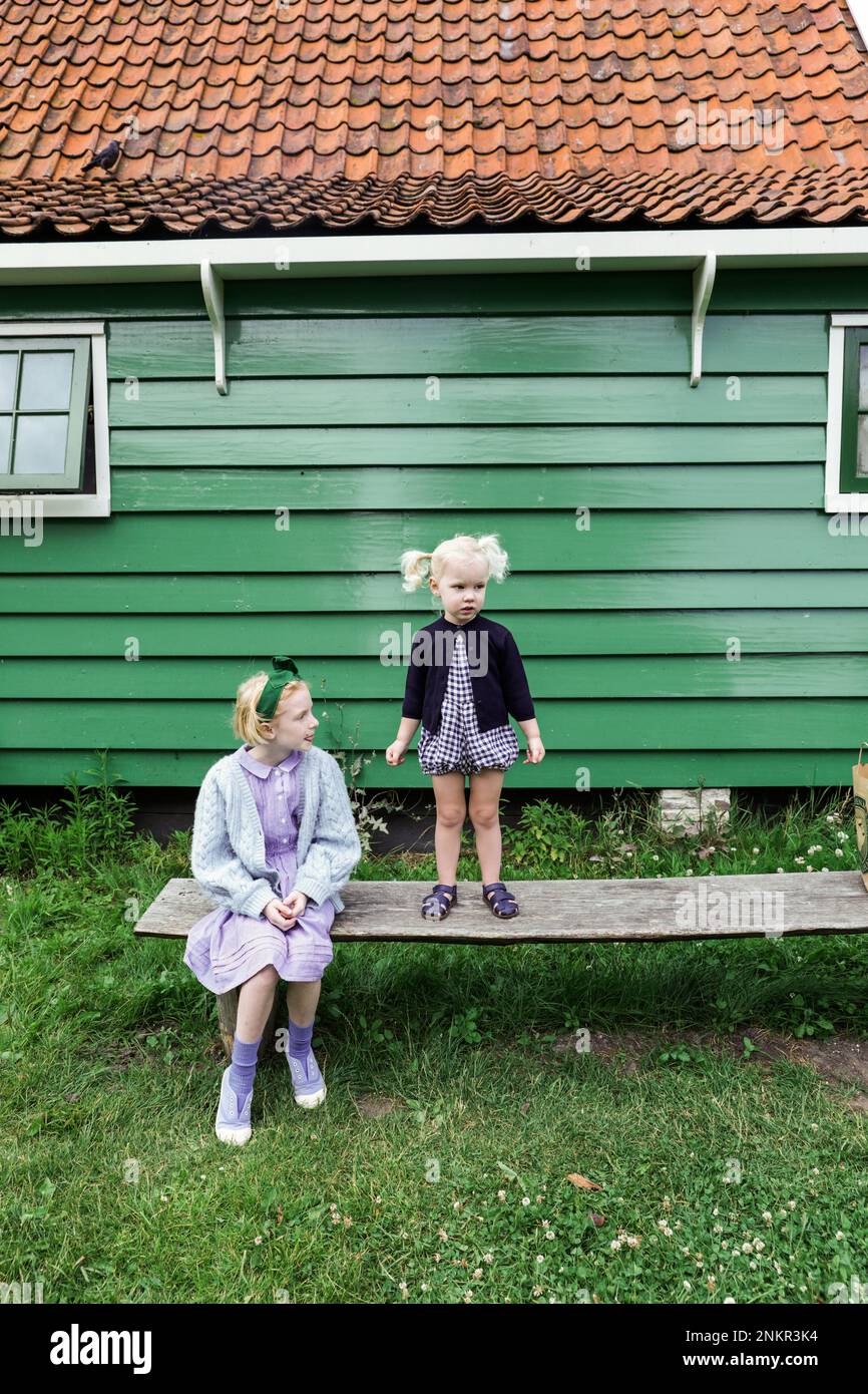 Deux filles à l'extérieur de la maison en bois, une debout et une assise sur le banc Banque D'Images