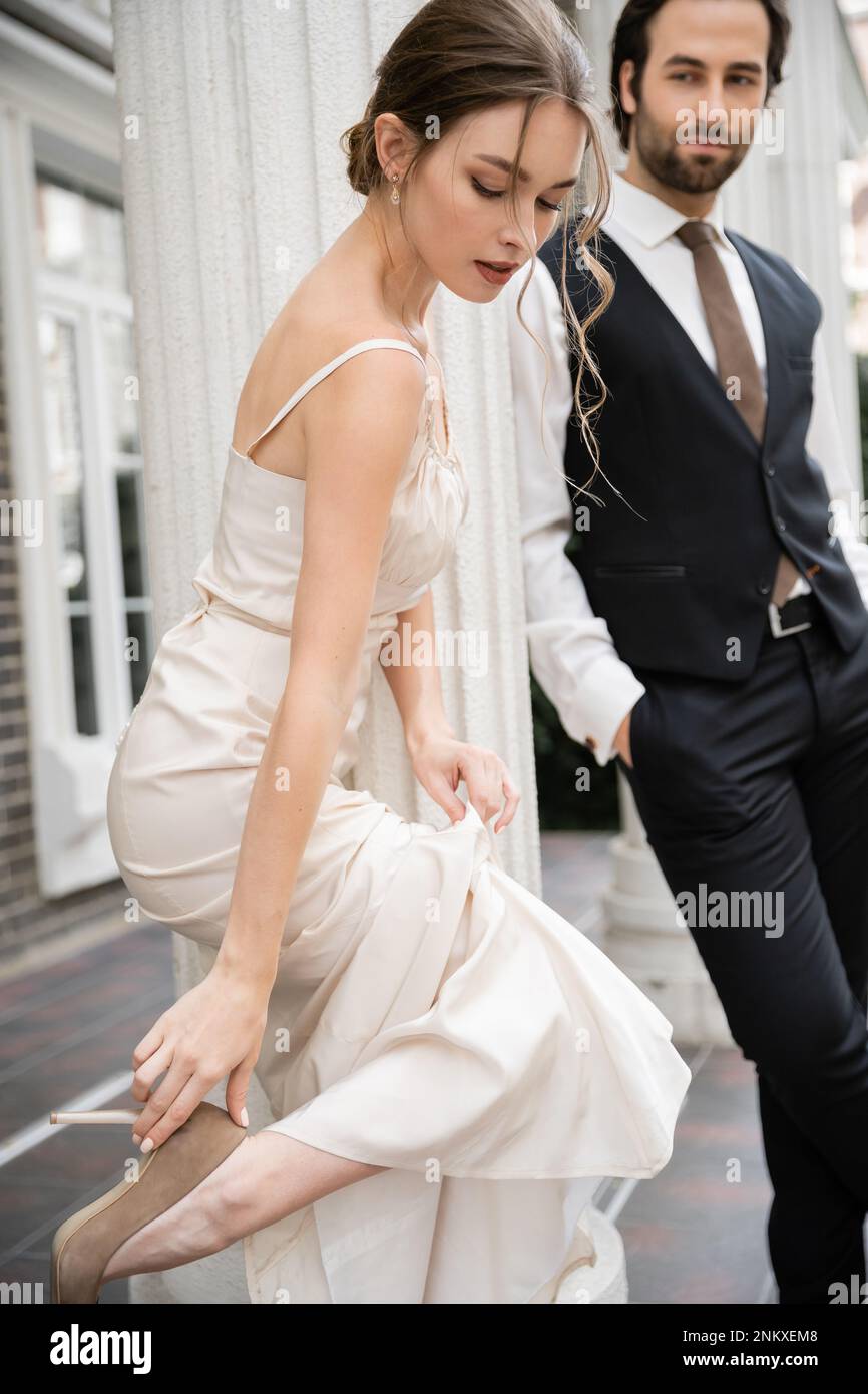 jolie mariée en robe de mariage portant une chaussure à talons hauts près du marié sur un arrière-plan flou, image de stock Banque D'Images