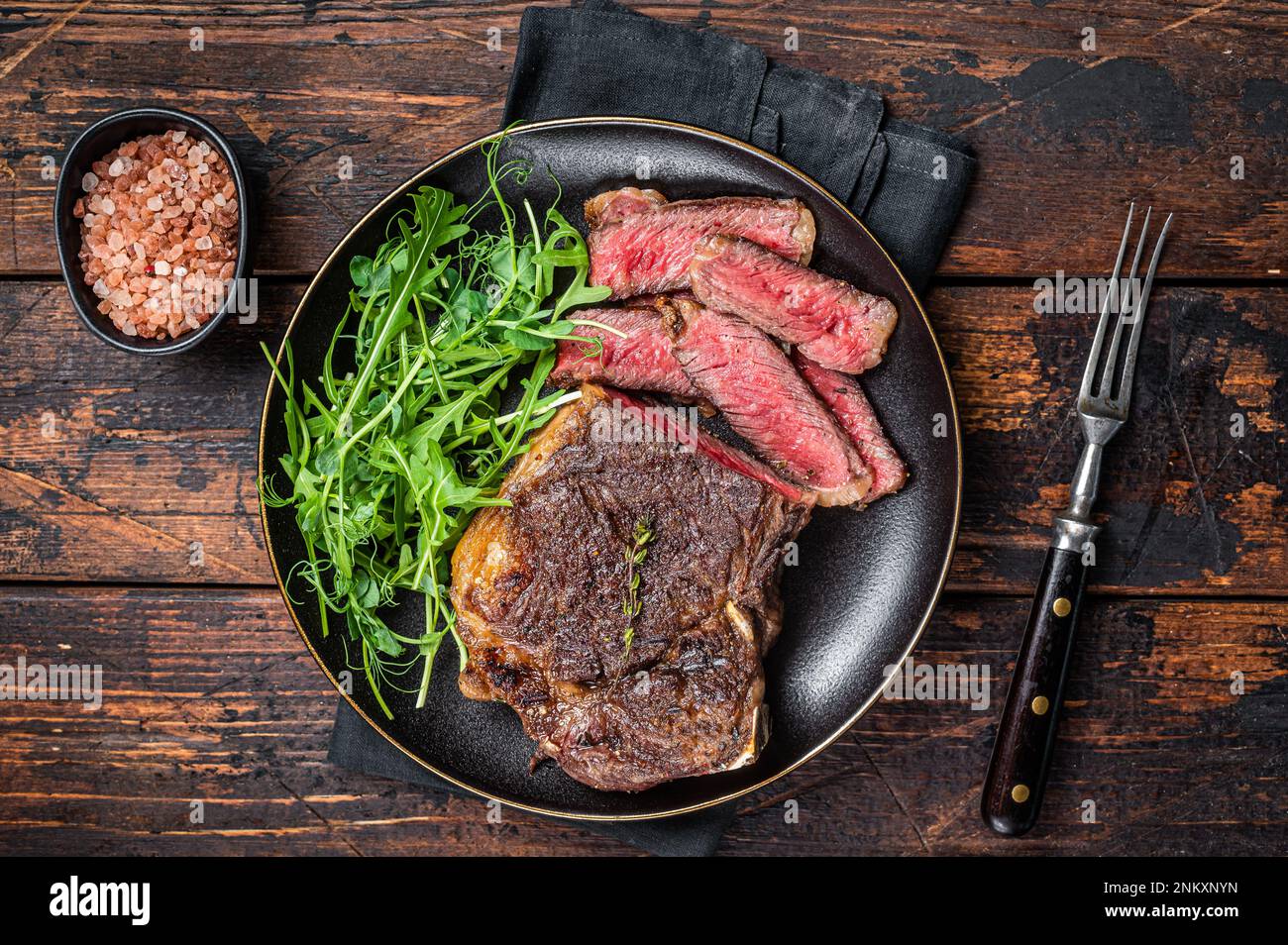 Steak de viande de bœuf Wagyu New York grillé au barbecue ou steak de stripline dans une assiette avec salade. Arrière-plan en bois. Vue de dessus. Banque D'Images