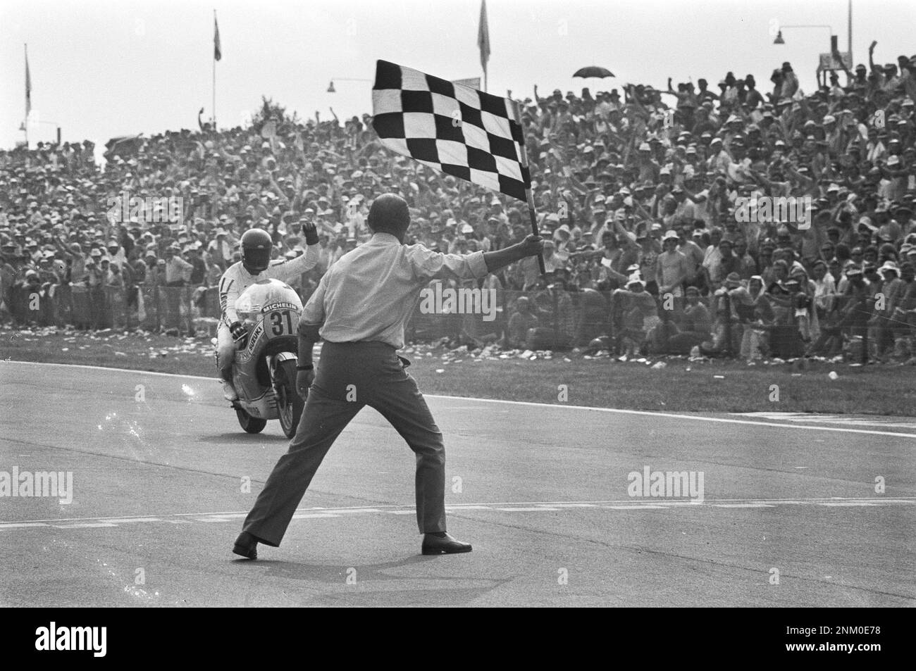 TT à Assen, course de moto de classe 500cc, homme agitant le drapeau à damier. Wil Hartog traverse la ligne d'arrivée à la troisième place ca. 26 juin 1976 Banque D'Images