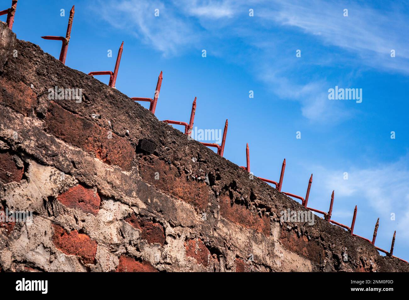 Mur de briques rouges avec pointes acérées sur le dessus. Ciel bleu clair avec nuages. Thème pour la prison et la liberté. Banque D'Images