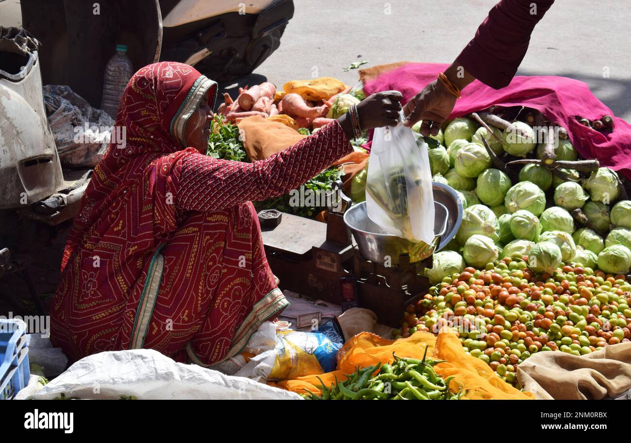 Une vendeuse de marché qui remet un sac de marchandises à un client alors qu'elle vend des fruits et des légumes de son magasin au bord du trottoir assis sur le sol Banque D'Images