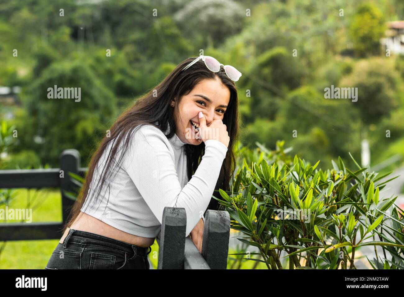 belle adolescente de latina, souriante tout en couvrant sa bouche avec sa main, penchée sur une vaya noire Banque D'Images