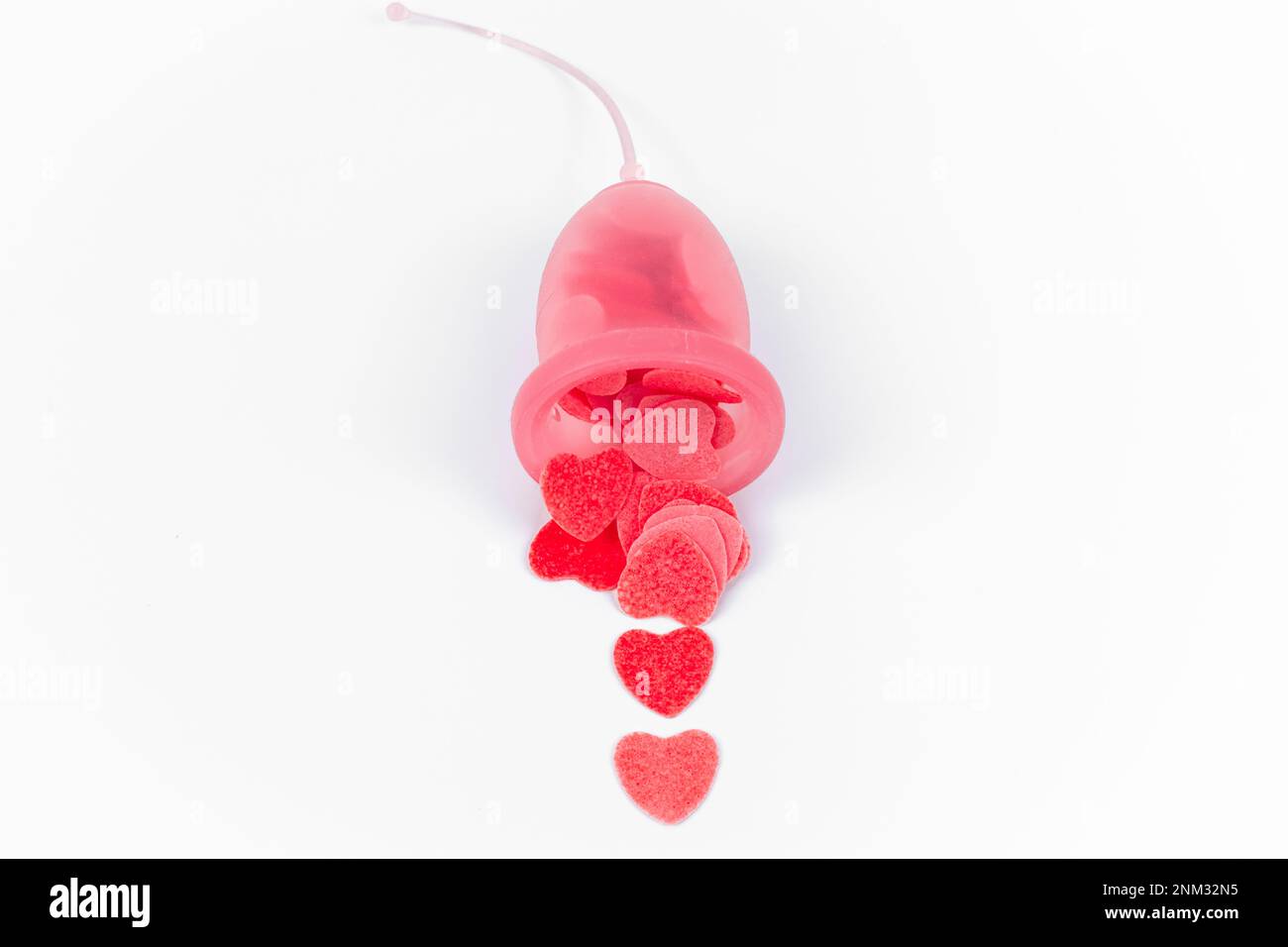 Tasse menstruelle rose pleine de petits coeurs rouges simulant le saignement. Produit d'hygiène intime féminin alternatif. La santé, la période et les saignements des femmes. Banque D'Images