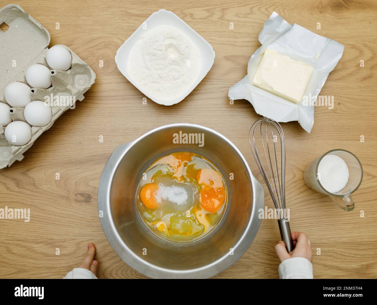 Mains d'enfant avec fouet. Oeufs, sucre, beurre, farine. Cuisson des ingrédients dans un bol, prêt à mélanger la pâte. Livre de cuisine. Banque D'Images