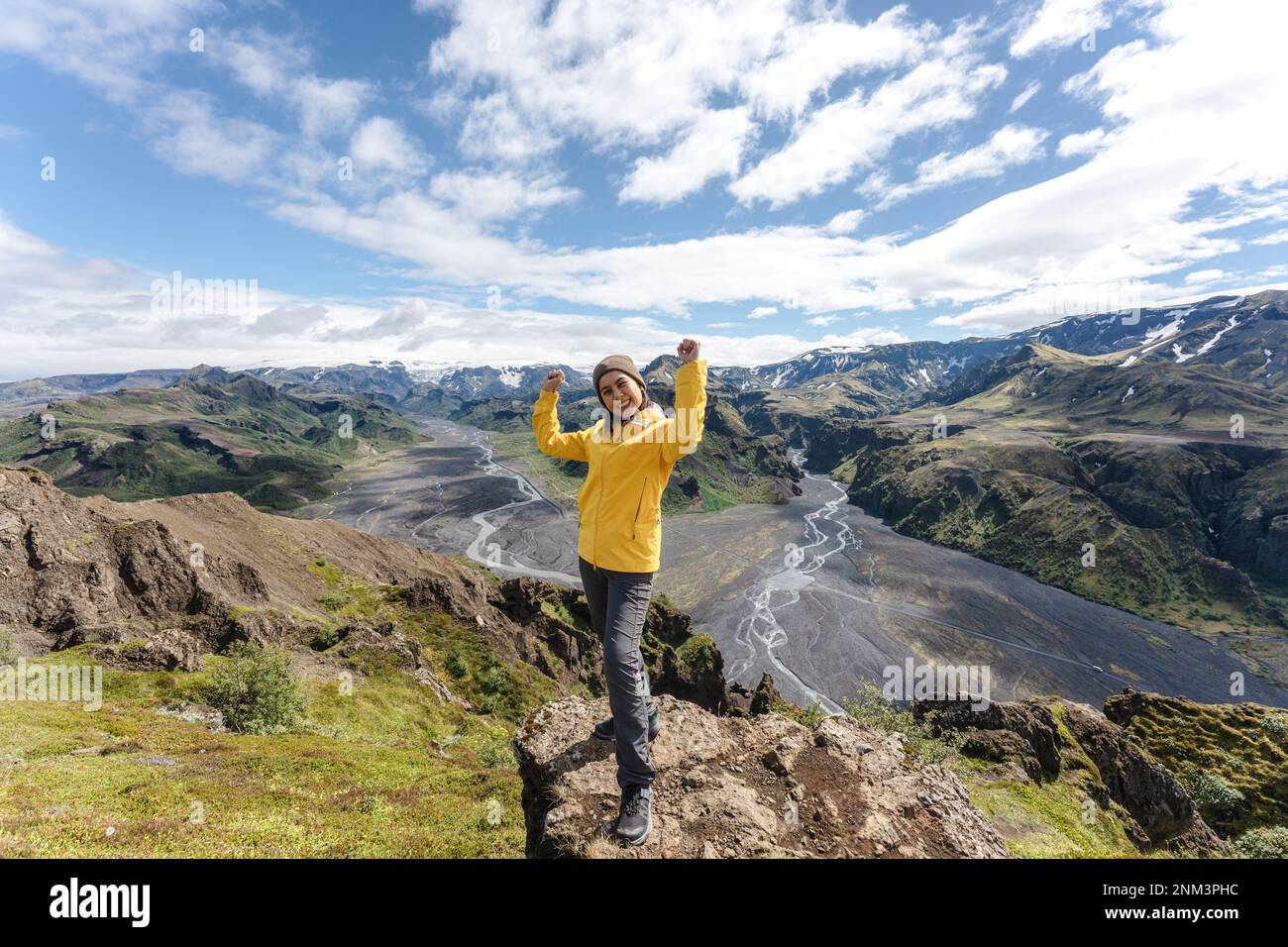 Succès du randonneur féminin dans une veste jaune debout et souriant au sommet de la montagne dans le point de vue de Valahnukur l'été à Thorsmork, Islande Banque D'Images