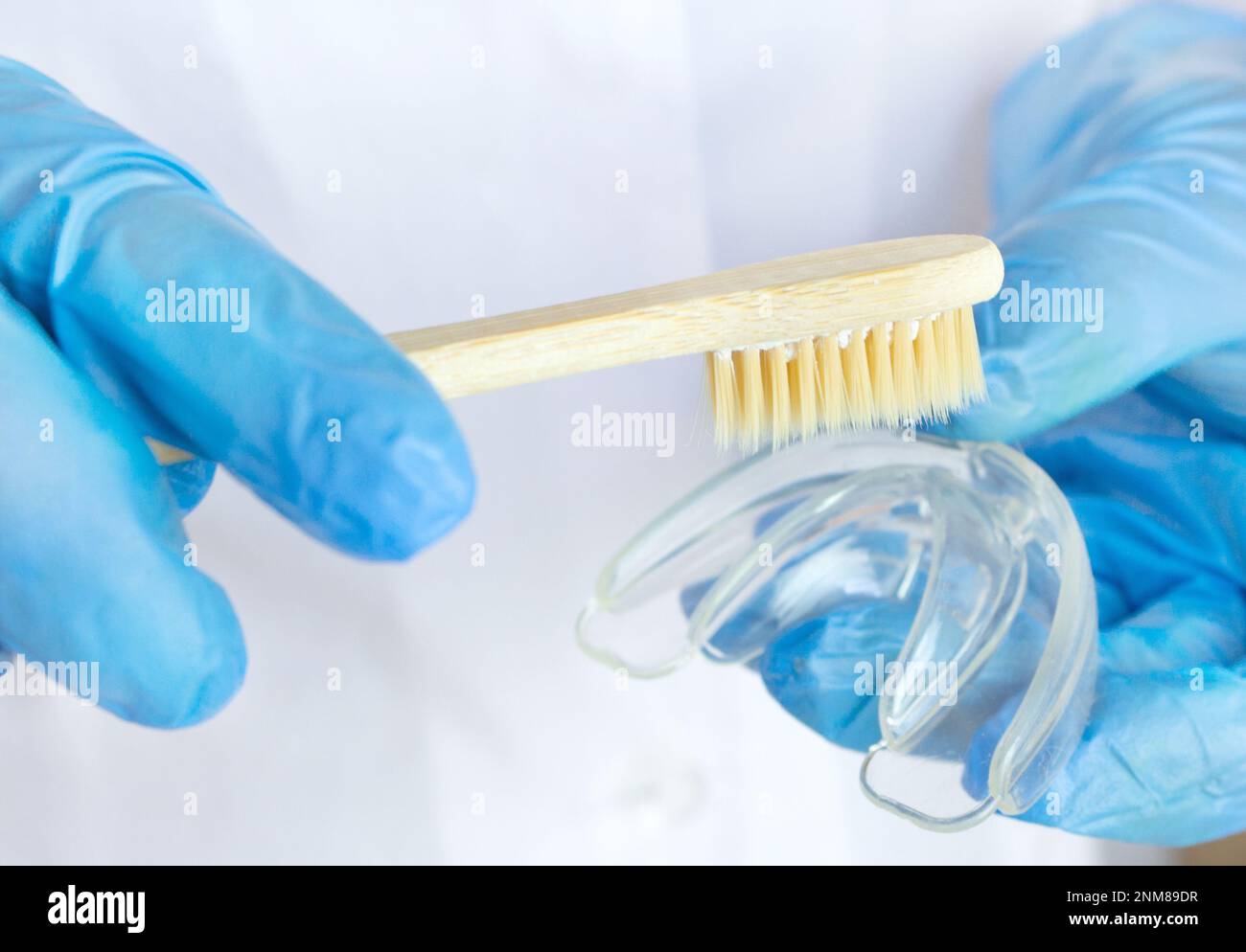 Dentiste insérant des dispositifs de retenue. Protège-dents avec brosse à dents en bois dans les mains des médecins gants bleus, orthodontique de l'adolescence, alignement dentaire clair Dora Banque D'Images