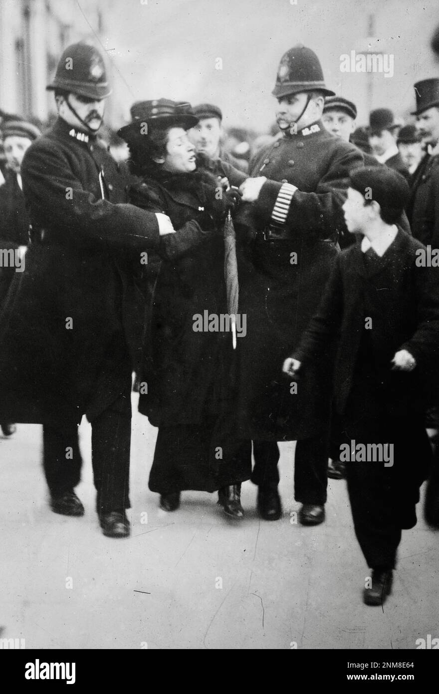 Deux barbys londoniens enterrés arrêtent une suffragette. Un jeune garçon regarde - 1910-1915 Banque D'Images