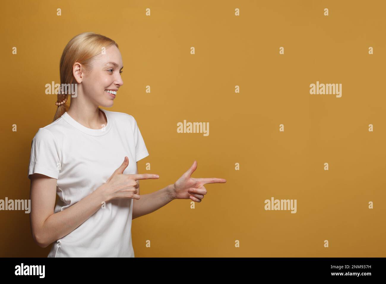 Souriante heureuse femme vendeur points au coin droit, a l'expression amicale du visage, porte décontracté t-shirt blanc isolé sur fond jaune Banque D'Images