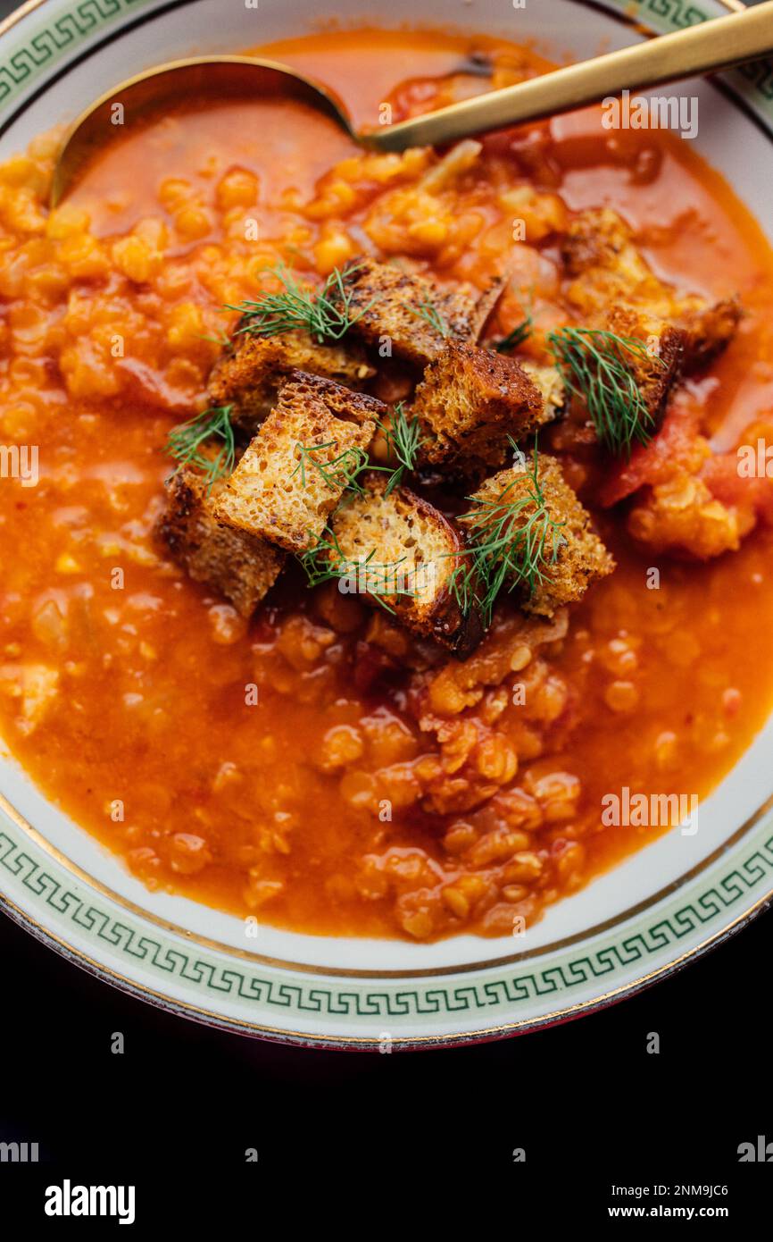 soupe de lentilles rouges et de tomates avec fenouil et croûtons dans un bol blanc avec clé grecque verte et cuillère dorée Banque D'Images