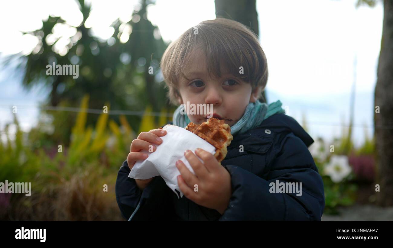 Un bon petit garçon mangeant des gaufres belges à l'extérieur. Un adorable garçon riant et souriant tout en mangeant de la nourriture de rue Banque D'Images