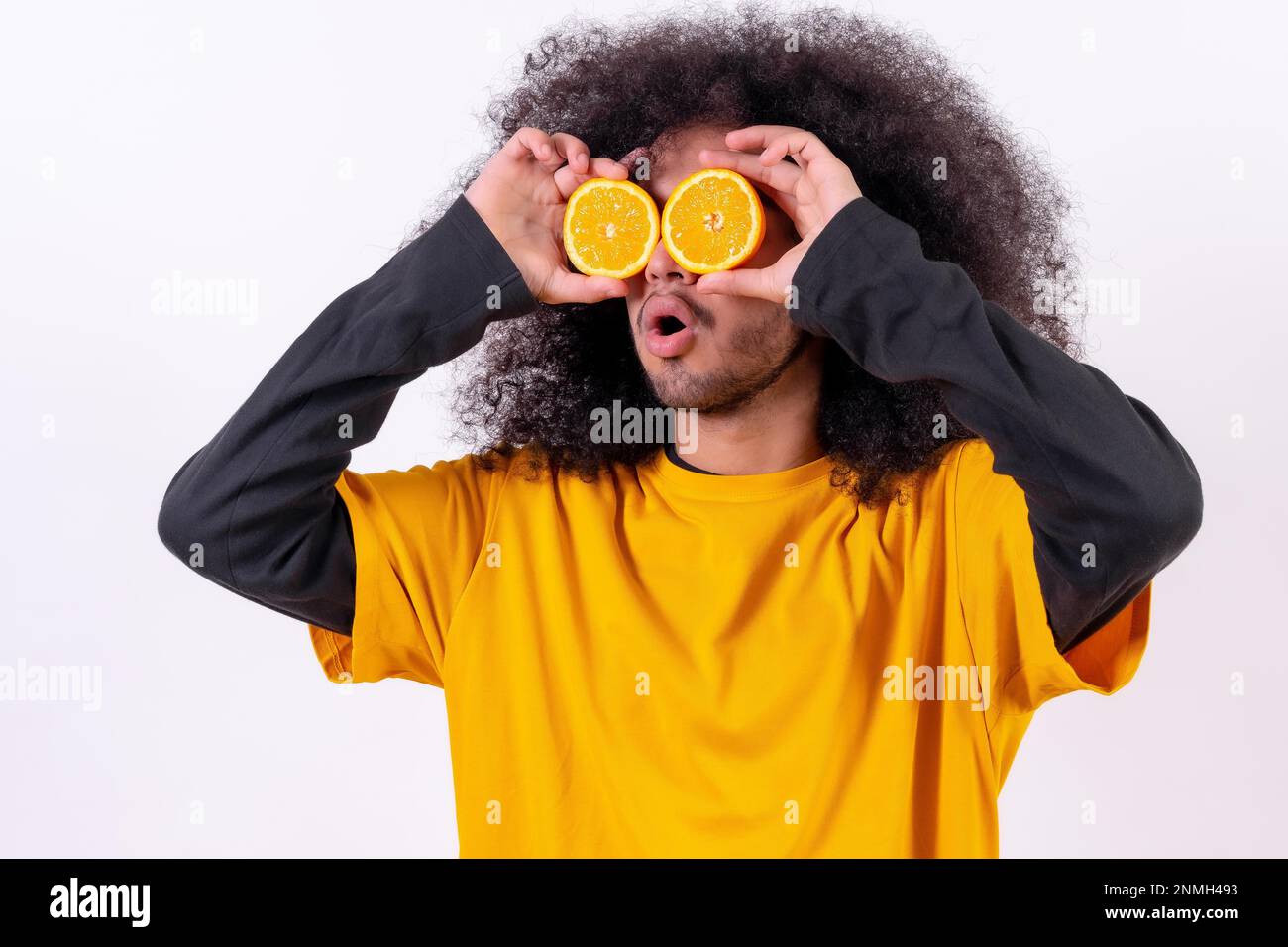 Portrait avec le fruit orange dans les yeux divisé en deux. Jeune homme avec cheveux afro sur fond blanc Banque D'Images