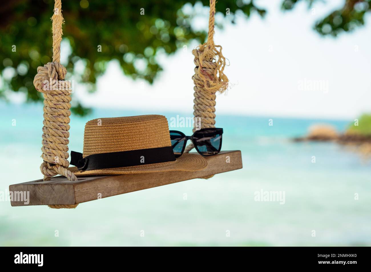 Accessoire de voyage tel qu'un chapeau, des lunettes de soleil sur une balançoire en bois couchée sous un arbre sur la plage de la mer, l'heure d'été, long week-end, vacances de voyage. Banque D'Images