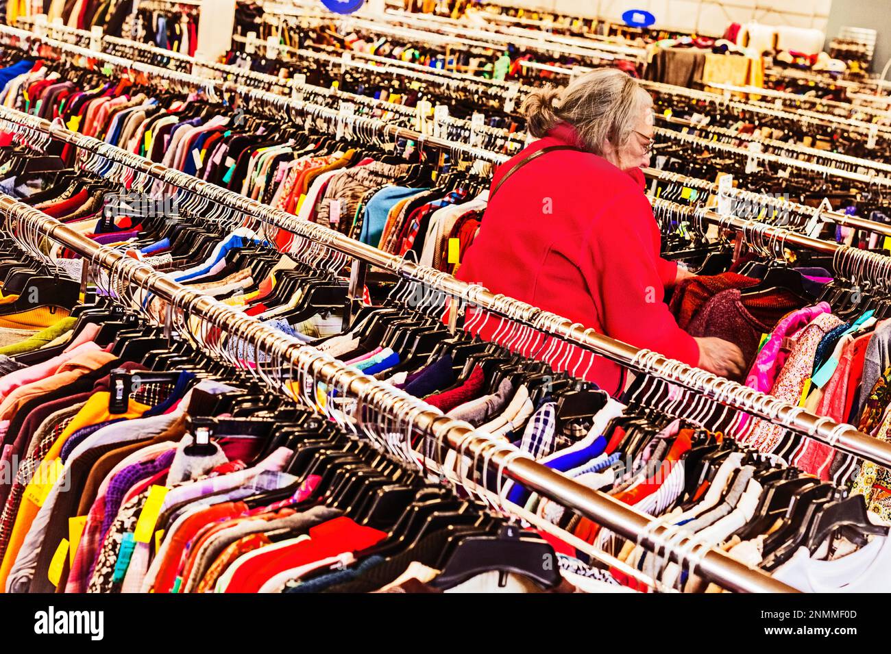 Femme âgée en blouson rouge traversant les porte-vêtements usagés à une rive thrift (bonne volonté) à Ludington, MI, États-Unis. Banque D'Images