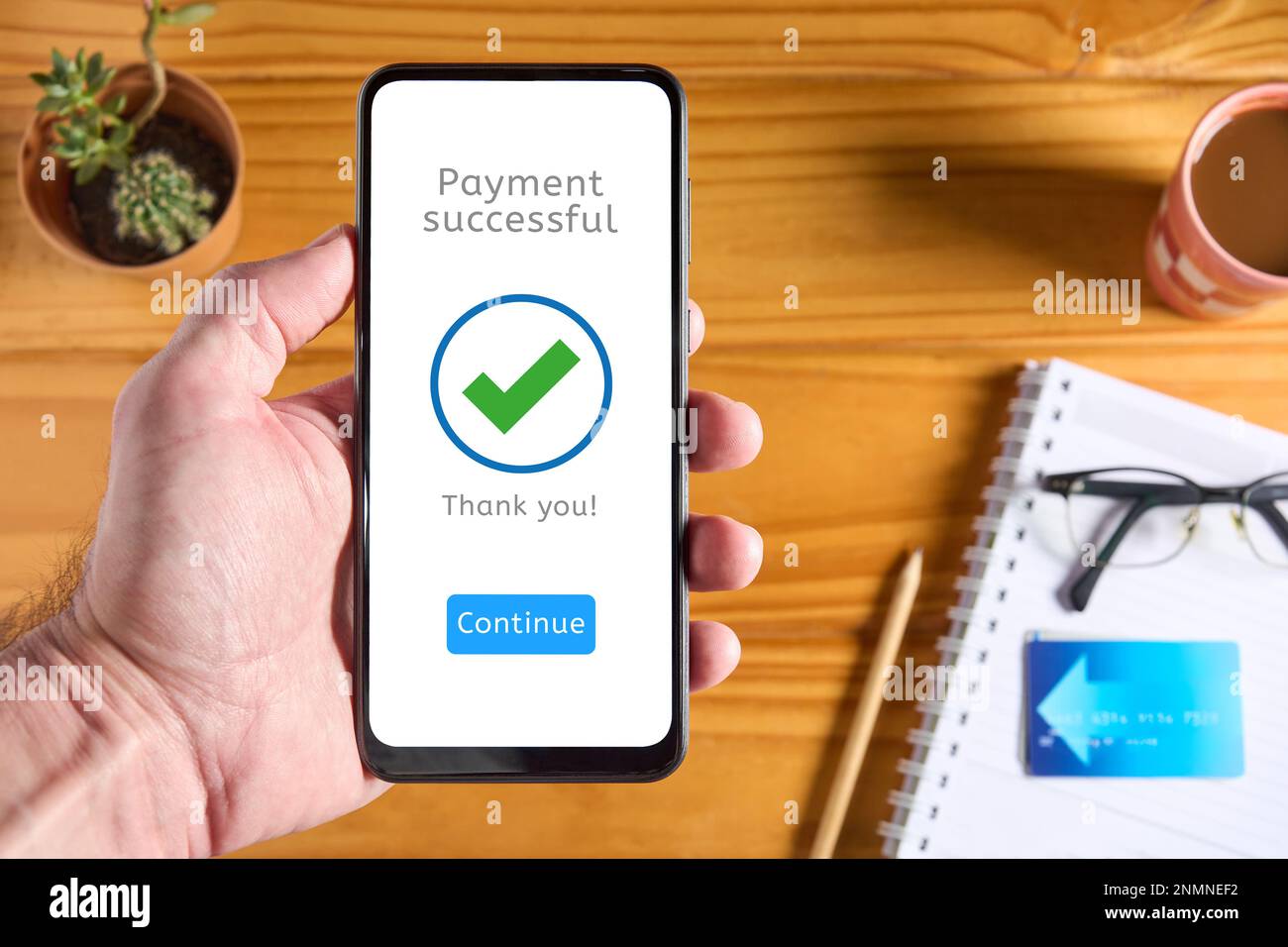 Téléphone portable de main d'homme avec interface d'application de paiement affichant un message indiquant que le paiement a réussi avec une coche verte. Carte de crédit en arrière-plan. Onl Banque D'Images