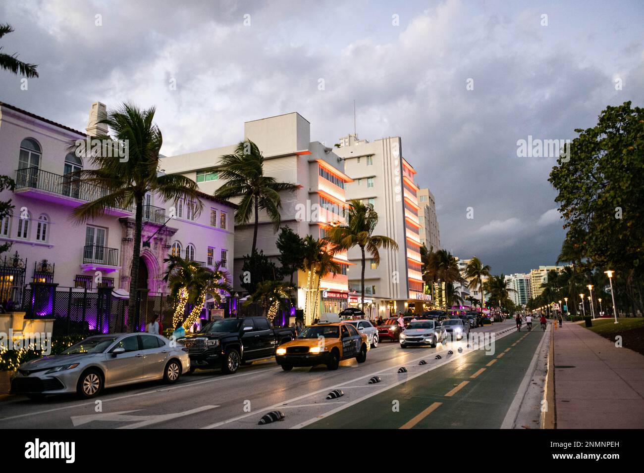 Photo du soir sur Ocean Drive dans le quartier de South Beach avec des gens qui font du vélo et de la marche tandis que les bâtiments s'illuminent. Banque D'Images
