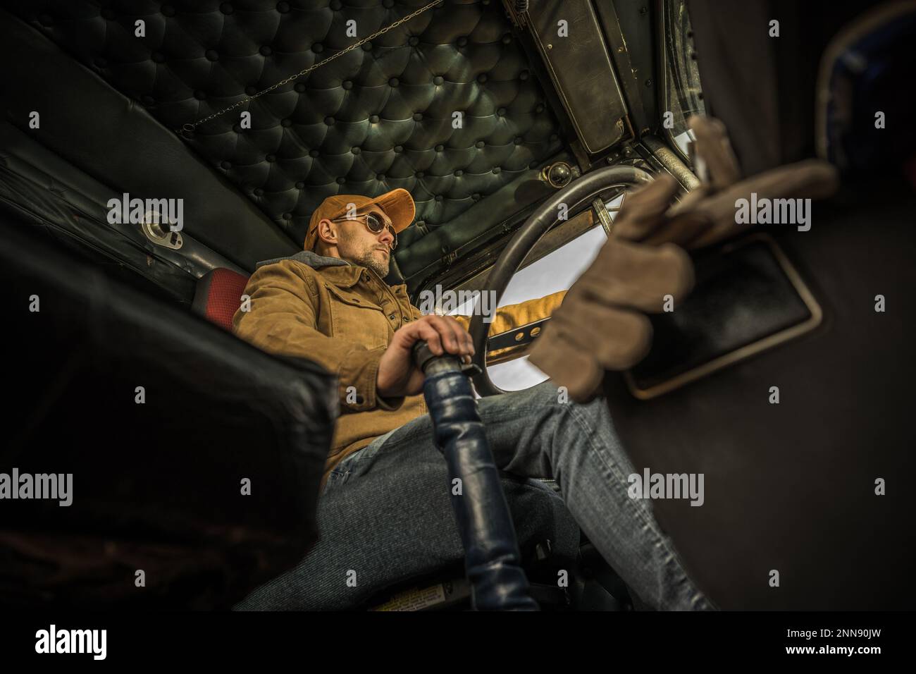 Professionnel caucasien Trucker conduisant son semi-camion américain. Vue de dessous de l'intérieur de la cabine. Banque D'Images