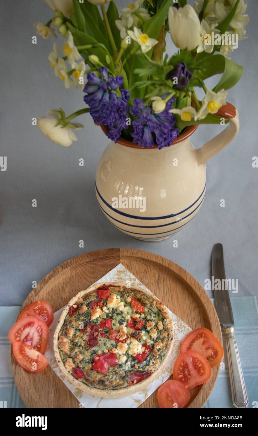 Quiche de poivre rouge et de légumes sur un plateau à côté d'une carafe de fleurs de printemps fraîches Banque D'Images