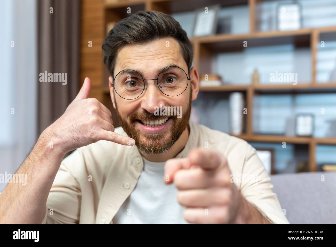 Gros plan. Portrait d'un jeune homme en lunettes parlant à l'appareil photo. Affiche et explique avec un geste de la main appelez-moi et pointe vers l'appareil photo. Banque D'Images