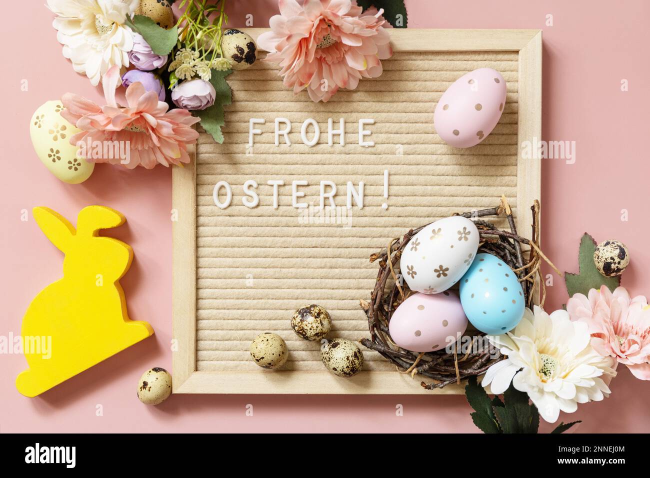 Tableau de lettres, Frohe Ostern - joyeuses Pâques en salutation allemande, oeufs de Pâques et fleurs de printemps sur fond rose pastel. Vue de dessus. Banque D'Images