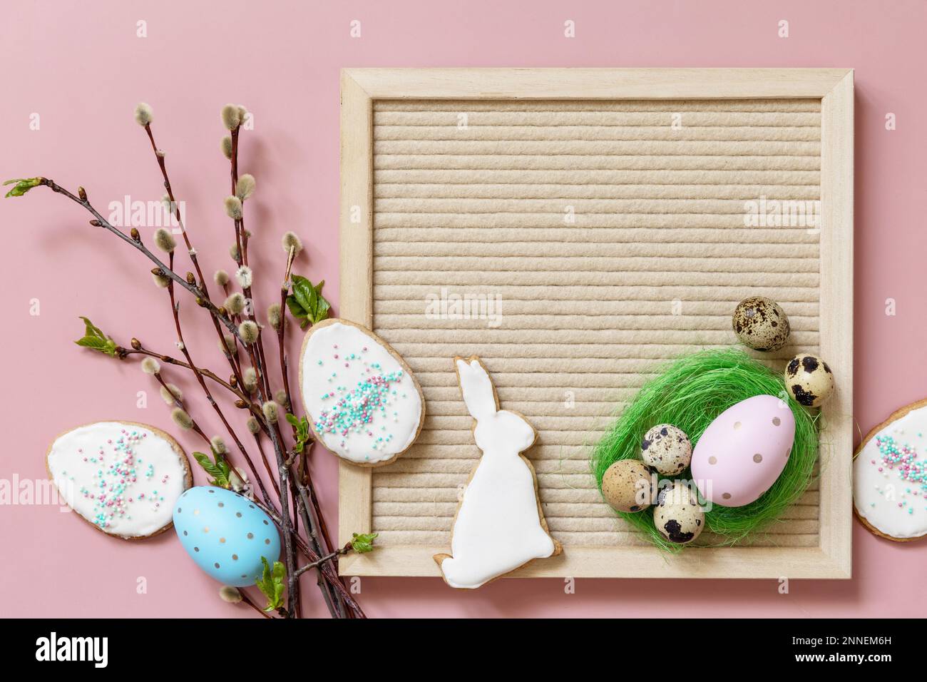 Disposition de bienvenue au printemps. Carton, œufs colorés et branches vertes sur fond rose, composition minimaliste. Vue de dessus. Banque D'Images