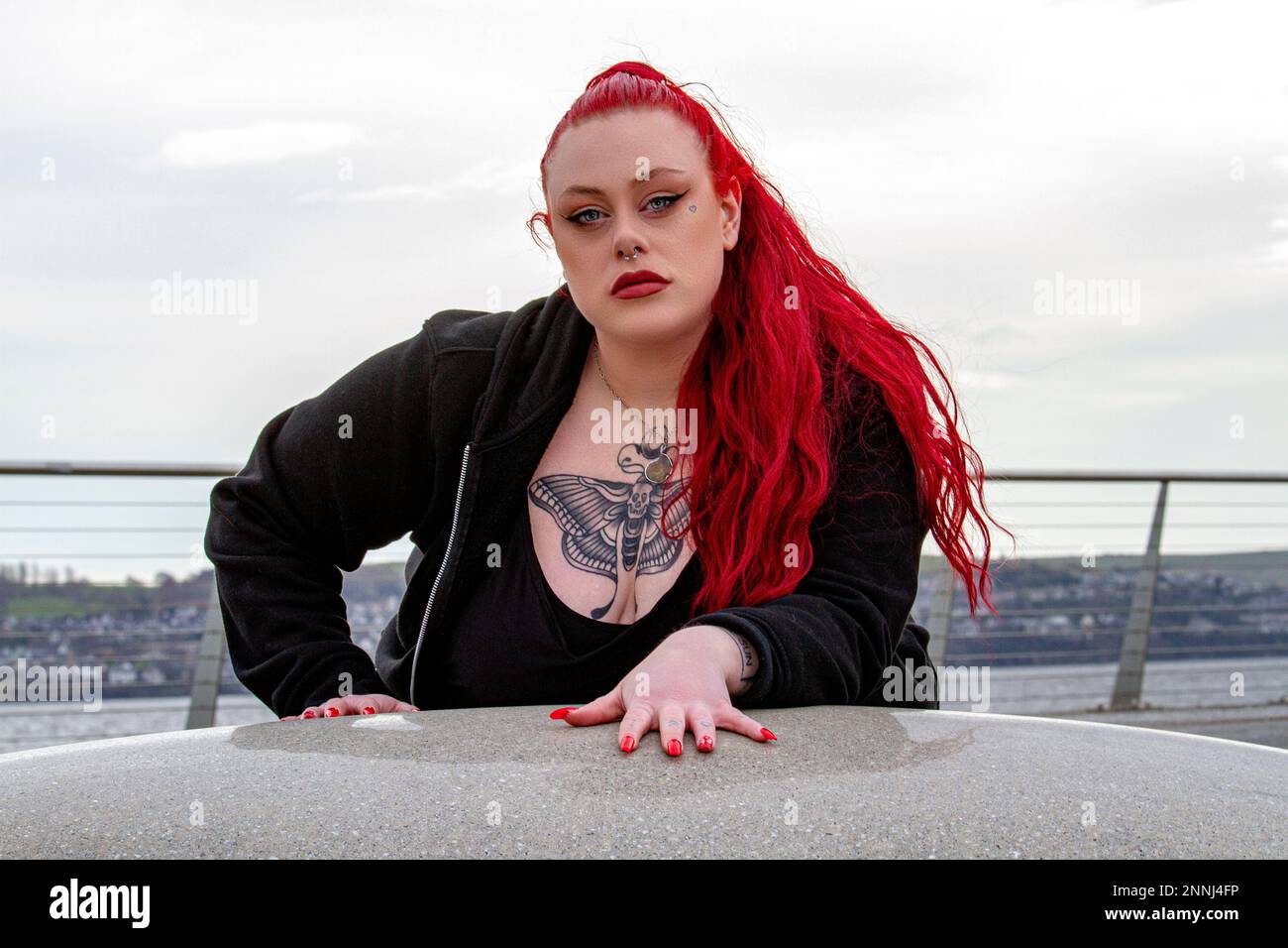 Une belle et sinueuse femme aux cheveux rouges pose pour la caméra le long du front de mer de Dundee dans un après-midi ensoleillé de février en Écosse Banque D'Images
