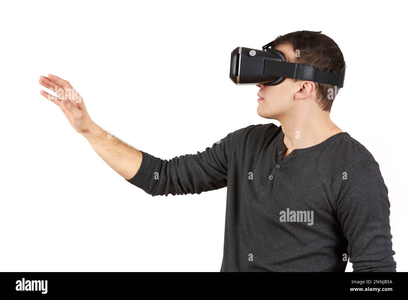 Un jeune homme avec un casque de réalité virtuelle sur sa tête tire sa main vers l'avant. La figure est isolée sur un fond blanc. Banque D'Images