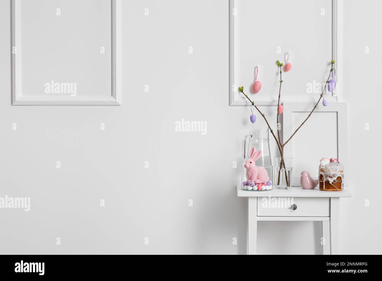 Magnifique décor de Pâques, gâteau et carafe d'eau sur la table près du mur lumineux Banque D'Images