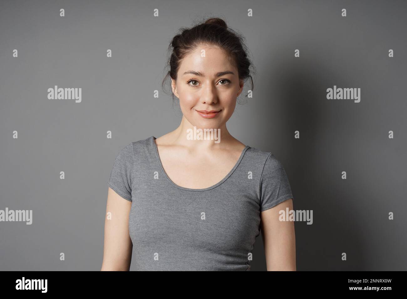 Content jeune femme d'une 20s avec le maquillage naturel et des cheveux brune chignon désordonné à plaisir Banque D'Images